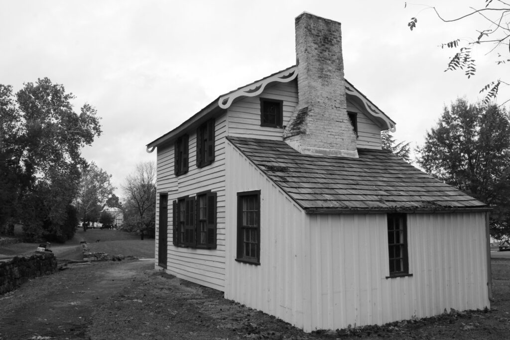 Image shows the southeast facade of the Innis house, a 19th century Civil War residence. The image is in black and white. The home is a quaint, massed plan with a saltbox addition. 