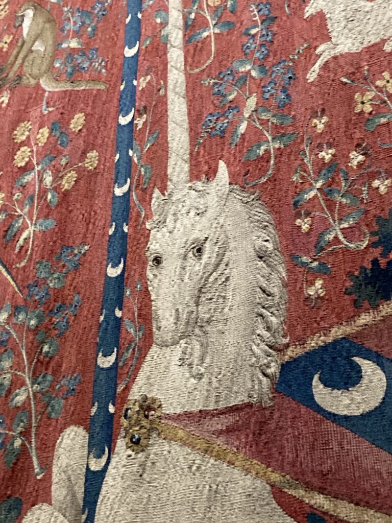 Mediaeval depiction of a Unicorn on a tapestry giving a side eye. 